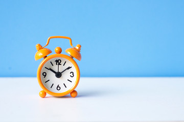 Orange alarm clock on blue pastel  background