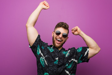 Young man wearing a vacation look celebrating a special day, jumps and raising arms with energy.