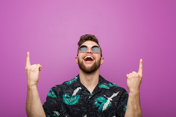 Young man wearing a vacation look indicates with both fore fingers up showing a blank space.