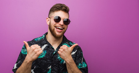 Young man wearing a vacation look raising both thumbs up, smiling and confident.