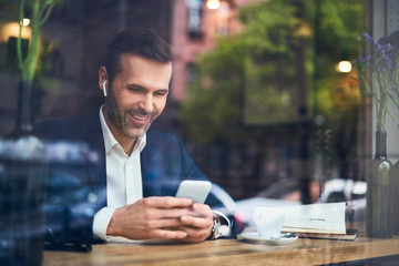 Businessman using phone with wireless headphones in cafe