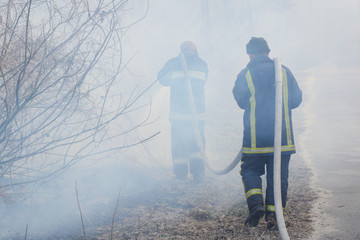 Two fireman in smoke battle forest fire. Brave firefighter goes into smoke to put down a wild fire,...