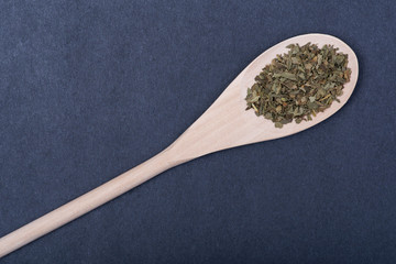Dried natural Basil spice (Ocimum basilicum) in handmade wooden spoon on dark background.