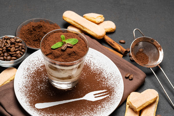Classic tiramisu dessert in a glass and cup of coffee on dark concrete background