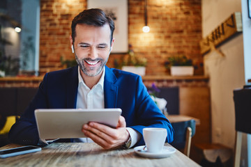 Portrait of businessman with wireless headphones using tablet in cafe