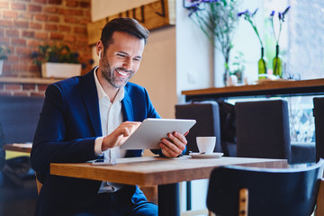 Businessman sitting in cafe using tablet and talking through wireless headphones - Powered by Adobe