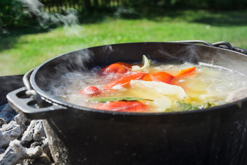 Shurpa soup in a large cast-iron cauldron outdoor. Summer food for hike. Turkish cuisine.