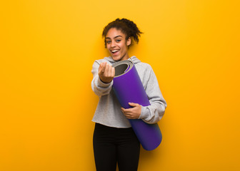 Young fitness black woman inviting to come. Holding a mat.