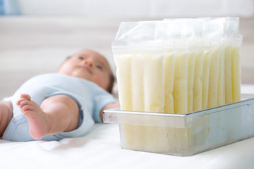 Breast milk frozen in storage bag and baby lying on background
