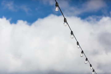 Lamp string hanging outside against a cloudy blue sky background