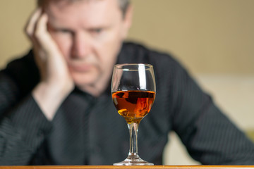 Tired man leaning his head on a glass of brandy. Man out of focus