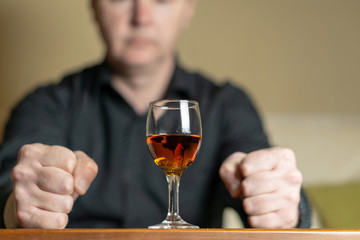 A man sits in front of a glass of brandy. Man out of focus