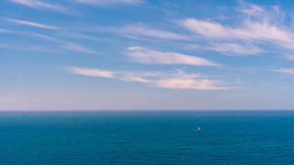 Naklejka na ściany i meble Seascape background with a sailboat navigating on a blue calm sea. 