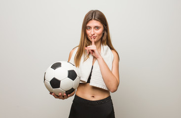 Young fitness russian woman keeping a secret or asking for silence. Holding a soccer ball.