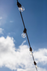 Lamp string hanging outside against a cloudy blue sky background