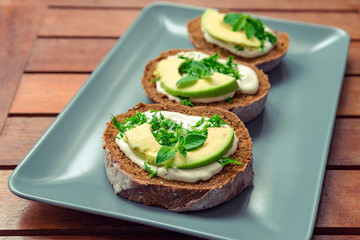Sandwiches with avocado, sour cream and greens on a gray plate on a wooden table