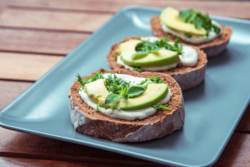Sandwiches with avocado, sour cream and greens on a gray plate on a wooden table
