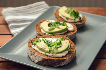 Sandwiches with avocado, sour cream and greens on a gray plate on a wooden table