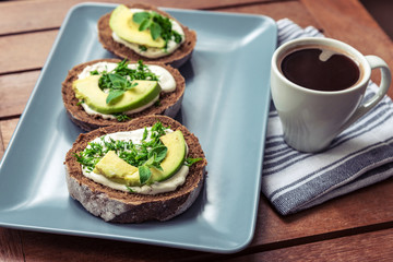 A cup of coffee and avocado sandwiches on a wooden table, healthy breakfast