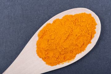 Turmeric powder in handmade wooden spoon on dark background. Curcuma longa of the ginger family.