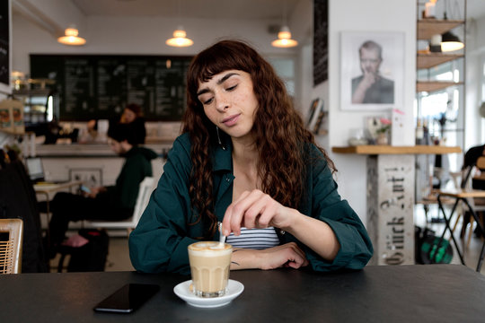 Young Woman With Milky Coffee Sitting At Table In A Cafe