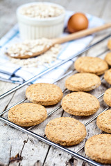 Baking grid with fresh oat cookies on rustic wooden table background, ingredients and kitchen utensil closeup.
