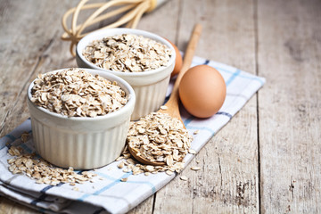 Fototapeta na wymiar Oat flakes in ceramic bowls and wooden spoon and fresh chicken eggs on rustic wooden table background.