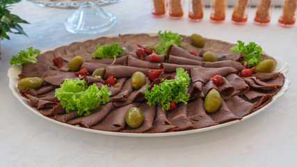 Appetizer tasty meat slim slices. Close up of banquette meat dish. Colorful restaurant meal with meat slices, green salad, olives. Banquette menu concept.