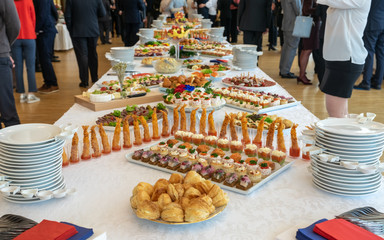 Banquette table setting. Delicatessen appetizers on long banquette table. Colorful delicious snacks on white covered table. Buffet party. Luxury banquette concept.