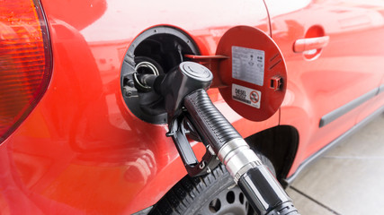 A red car is at a gas station and is fueled with diesel. Closeup of the tap and the tank.