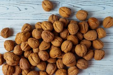WALNUT NUTS IN A SHELL SPREADED ON A WHITE WOODEN BACKGROUND FLAT LAY