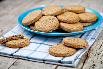 Fresh baked oat cookies on blue ceramic plate on linen napkin on rustic wooden table.