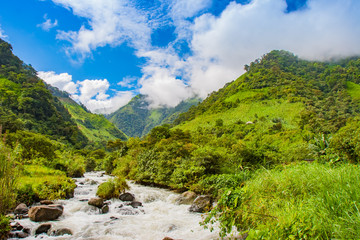 Fototapeta na wymiar South America. Ecuador. Ecuadorian Andes with tops covered with clouds. Rough Pastaza river at the foot of the mountains. Mountain landscape of Ecuador. Extreme tours in Ecuador.