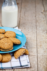 Fototapeta na wymiar Fresh baked oat cookies on blue ceramic plate on linen napkin and bottle of milk on rustic wooden table background.