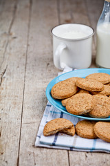 Fresh baked oat cookies on blue ceramic plate on linen napkin and cup of milk on rustic wooden table background.