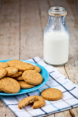 Fresh baked oat cookies on blue ceramic plate on linen napkin and bottle of milk on rustic wooden table.