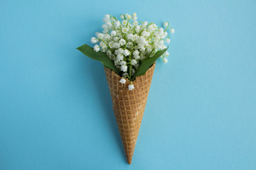 Ice cream cone with lilies of the valley  in the center of the blue background.Top view.Copy space.Spring flowers concept.
