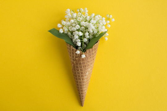 Ice cream cone with lilies of the valley  in the center of the yellow  background.Top view.Copy space.Spring flowers concept.