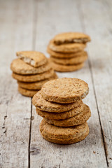 Three stacks of fresh baked oat cookies on rustic wooden table.