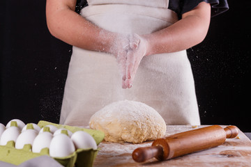 young woman in apron kneading dough on board