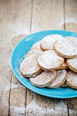 Fresh baked oat cookies with sugar powderon blue ceramic plate closeup on rustic wooden table background.