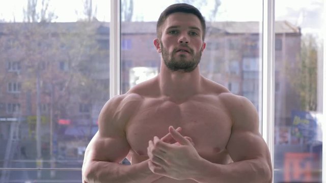sports lifestyle, beautiful strong bodybuilder man does warm-up after power workout in building muscle in fitness center against window