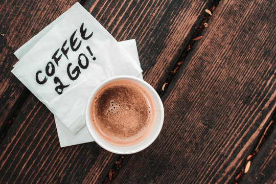White cup of coffee sitting on a white napkin with the message coffee 2 go hand written on it placed on a wooden board – Concept image for fast break or fast lifestyle