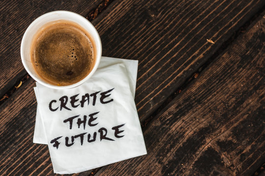 Full cup of coffee with foam sitting on white napkin with the message create the future hand written on it placed on a wooden surface – Concept image for inspirational messages