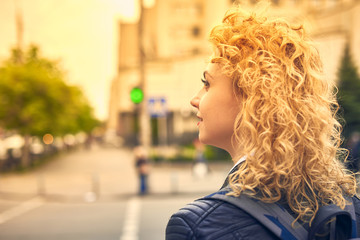 curly blond young woman crossing the street on a green light of traffic light
