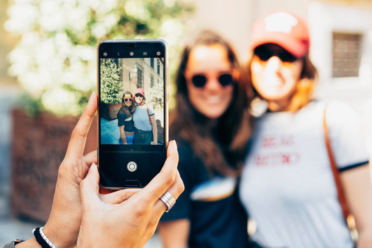 Girl's hands taking photo with a smartphone of a happy women lesbian couple in Madrid. Same sex relationship and real love concept.