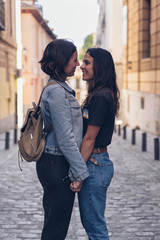 Attractive young women lesbian couple looking and smiling each other in a street of Madrid. Real love scene.