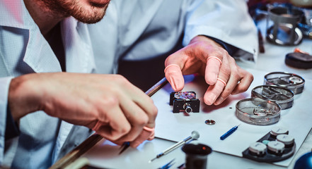 Undistracted clockmaster is fixing old watch for a customer at his own workshop.