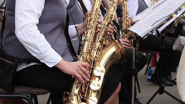 Women musicians play saxophones in municipal orchestra performing at festive concert open air.