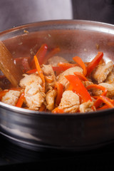 young woman in a gray aprons roasts chicken fillet with carrots